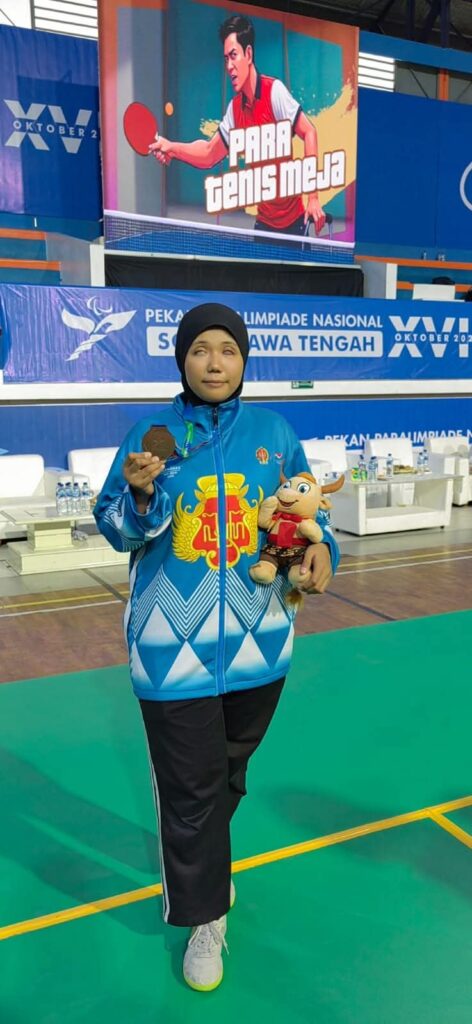 Gambar ini menunjukkan seorang wanita muda berhijab yang memegang medali dan boneka. Dia tersenyum dan tampak gembira. Wanita ini mungkin adalah seorang atlet yang baru saja memenangkan medali.